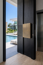 Timber-look aluminium pivot front door with oversized offset pivot system, concealed floor spring, and brushed brass flush handle, designed for modern coastal luxury homes