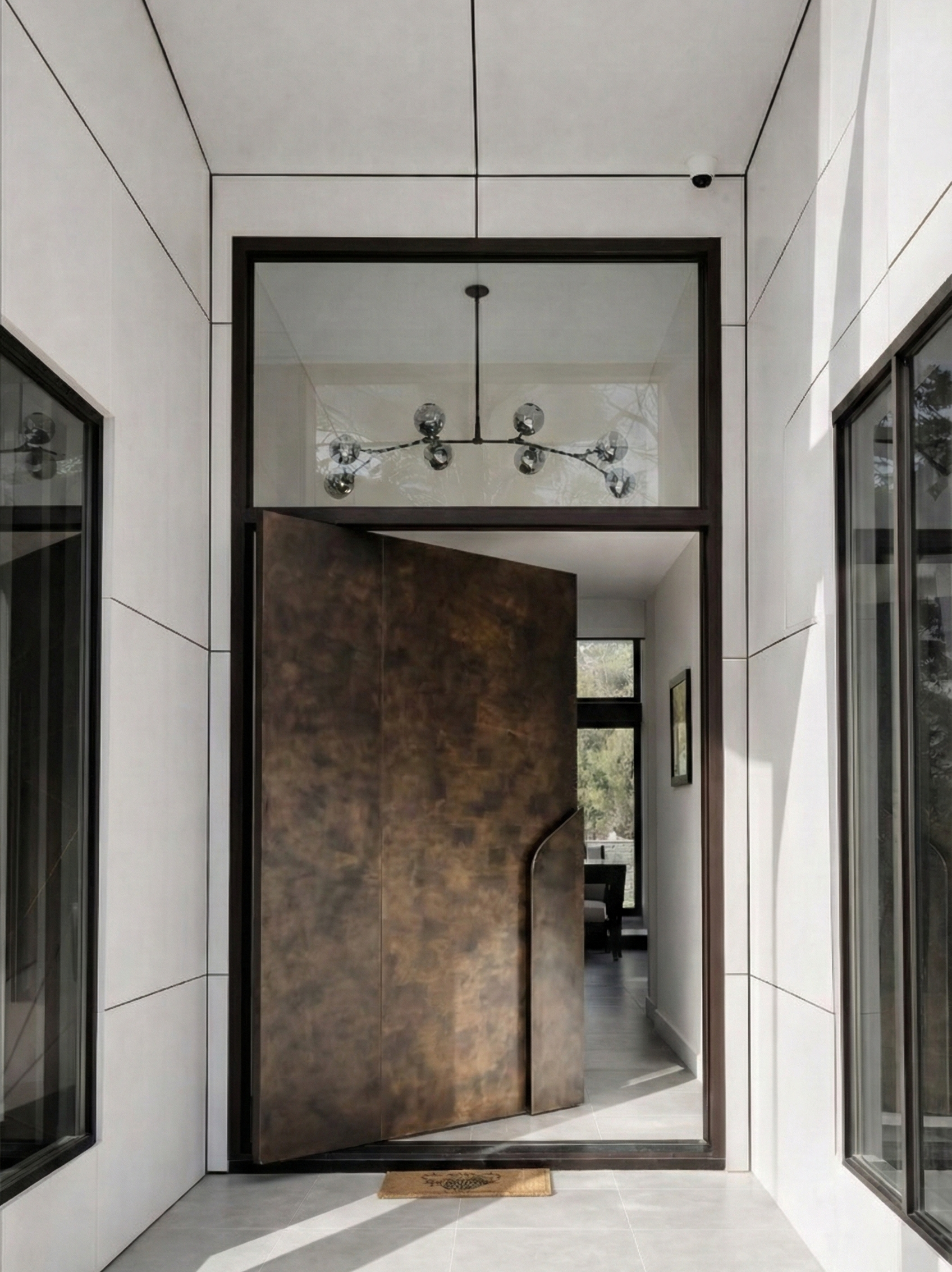 Bronze finish aluminium pivot door with concealed frame and custom sculptural pull handle in modern luxury entrance