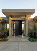 Large cast aluminium pivot door at modern stone facade home entrance
