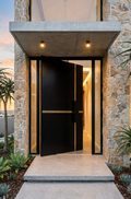 Black cast aluminium pivot door at modern stone facade home entrance

